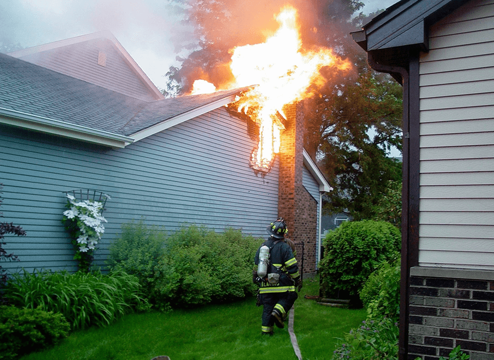 A fireman is in the yard with a hose.